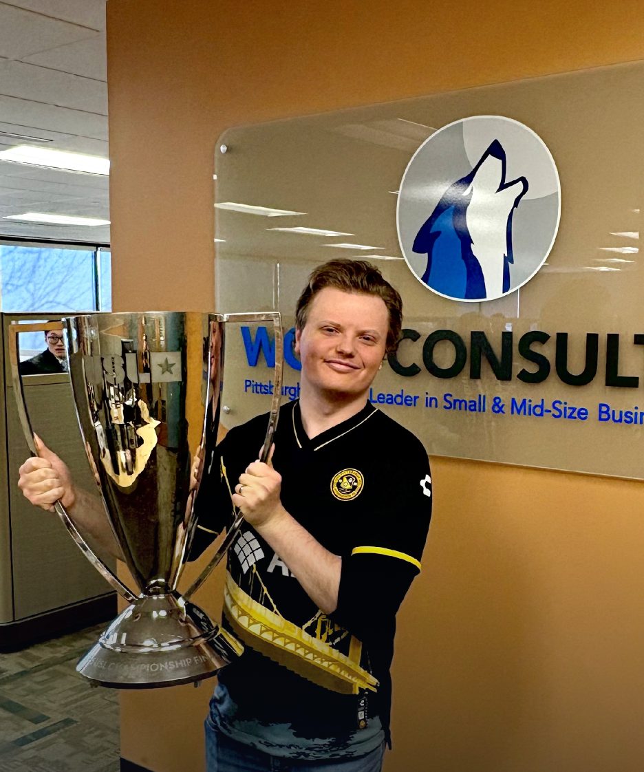 A Wolf Consulting team member holding a championship trophy by the office logo wall